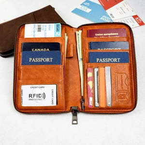 May include: Open, orange leather travel wallet with multiple compartments. The wallet is filled with passports, credit cards, and cash. The wallet has a zipper closure and RFID protection.