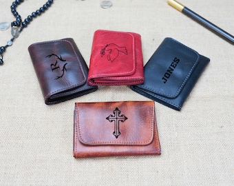 May include: Four different leather wallets with various designs. One wallet has a cross, one has a dove, one has a deer, and one has the name "JONES" engraved on it.