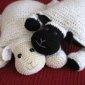 May include: Two crocheted sheep plushies, one white and one black, lying next to each other on a red surface. The white sheep has a brown nose and black eyes. The black sheep has a white nose and black eyes.