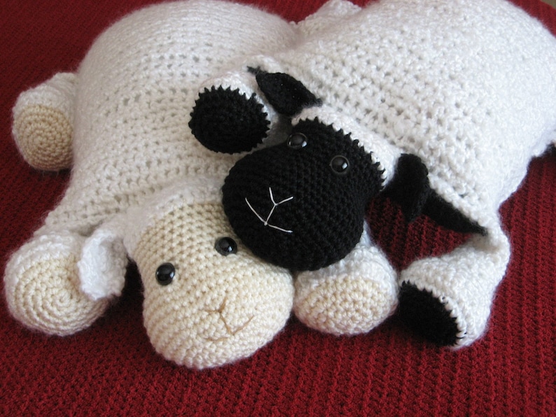May include: Two crocheted sheep plushies, one white and one black, lying next to each other on a red surface. The white sheep has a brown nose and black eyes. The black sheep has a white nose and black eyes.