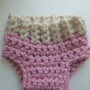 May include: A pink and white crocheted diaper cover. The diaper cover is made with a soft, chunky yarn and has a simple, classic design.