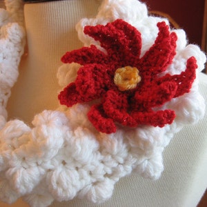 May include: A white crocheted scarf with a red crocheted flower accent. The flower has a yellow centre.