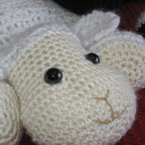 May include: A white crocheted lamb with black button eyes. The lamb has a stitched-on nose and mouth.