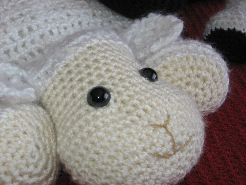 May include: A white crocheted lamb with black button eyes. The lamb has a stitched-on nose and mouth.
