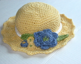 May include: A yellow crocheted sun hat with a white trim and blue and yellow crocheted flowers.
