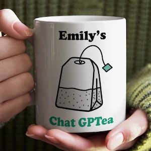 May include: White ceramic mug featuring the text "Emily's Chat GPTea" and a tea bag illustration. The mug is held by a person wearing a green sweater. The tea bag graphic is black and white with a teal tag.