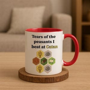 May include: White ceramic mug with a red interior and handle. The mug features the text "Tears of the peasants I beat at Catan" and a graphic of resource icons from the board game Catan.