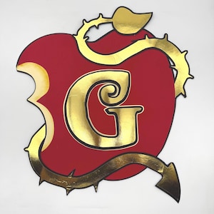 May include: A red apple-shaped design featuring a gold letter "G". The apple has a bite taken out of it, and is encircled by a gold vine with thorns. The design is set against a white backdrop.