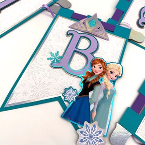 May include: A banner with a white background and snowflake pattern, featuring the letter "B" in purple, a silver crown, and images of two cartoon characters. The banner has teal and purple accents.