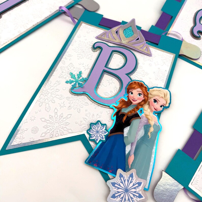 May include: A banner with a white background and snowflake pattern, featuring the letter "B" in purple, a silver crown, and images of two cartoon characters. The banner has teal and purple accents.
