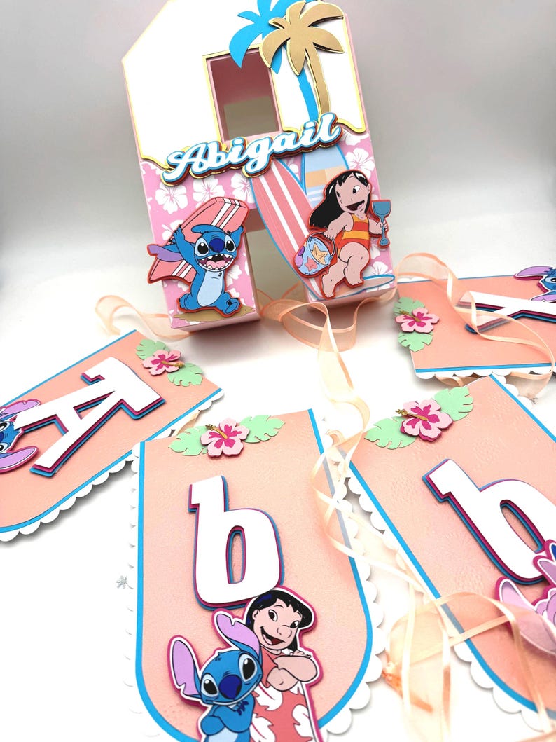 May include: A custom party decoration with a tropical theme. The centerpiece is a white and pink house-shaped box with the name "Abigail". The box is decorated with cartoon characters, surfboards, and a palm tree. A banner spells out "Abigail".