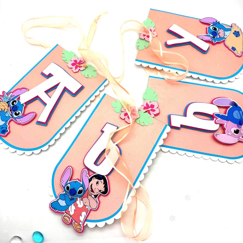 May include: A custom banner spelling "KAYLA" on pink pennants. Each pennant has a white scalloped edge, blue trim, and a cartoon character design. The banner is decorated with flowers and a light yellow ribbon.