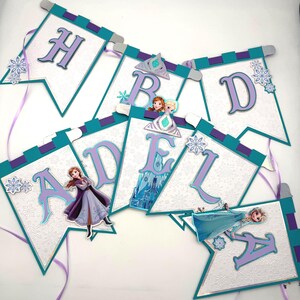 May include: A banner with the letters "HBD ADELA" in purple, teal, and white. Each pennant features a snowflake design and images of characters from the movie Frozen. The banner is decorated with purple ribbons.