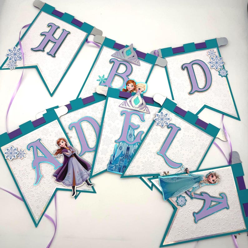May include: A banner with the letters "HBD ADELA" in purple, teal, and white. Each pennant features a snowflake design and images of characters from the movie Frozen. The banner is decorated with purple ribbons.