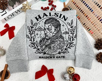 May include: A grey sweatshirt with a black embroidered design featuring a character named Halsin from the game Baldur's Gate. The design includes a wreath of leaves, clouds, and stars.