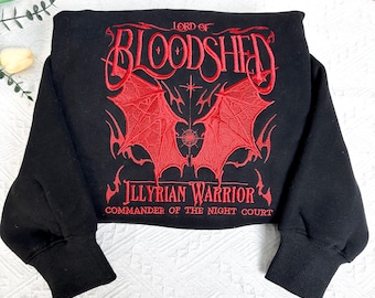 May include: Black sweatshirt with a red embroidered design featuring a pair of wings and the text "Lord of Bloodshed Illyrian Warrior Commander of the Night Court".