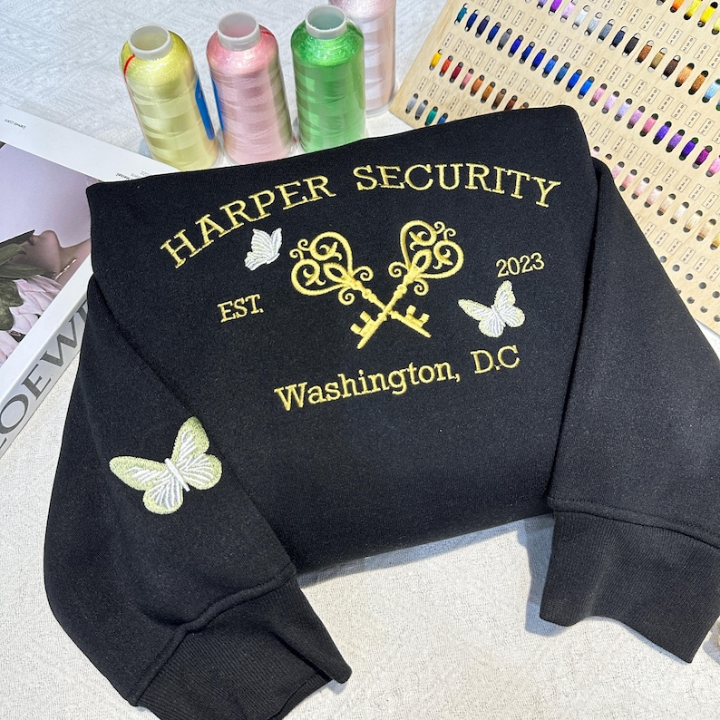 May include: Black sweatshirt with gold embroidery of two keys crossed, butterflies, and the text "HARPER SECURITY EST. 2023 Washington, D.C."