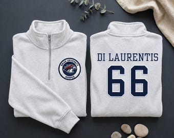 May include: Two light gray quarter-zip sweatshirts. One features a Briar University Hawks logo on the front. The other has "DI LAURENTIS" and the number "66" in navy blue. The sweatshirts are displayed on a dark gray surface.