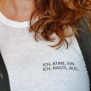 May include: White t-shirt with black text that reads "ICH. ATME. EIN. ICH. RASTE. AUS."