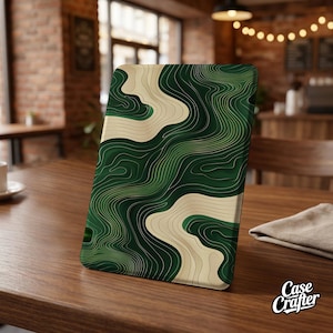 May include: A green and cream topographic design adorns a rectangular product, possibly a tablet case. The design features layered lines in varying shades of green and cream, creating a textured, abstract pattern. The product is displayed on a wooden table.