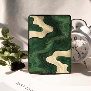 May include: A black tablet case with a green and beige topographic design. The case has a modern look with a detailed, layered pattern. The design resembles a map with contour lines. The case is displayed on a white surface.