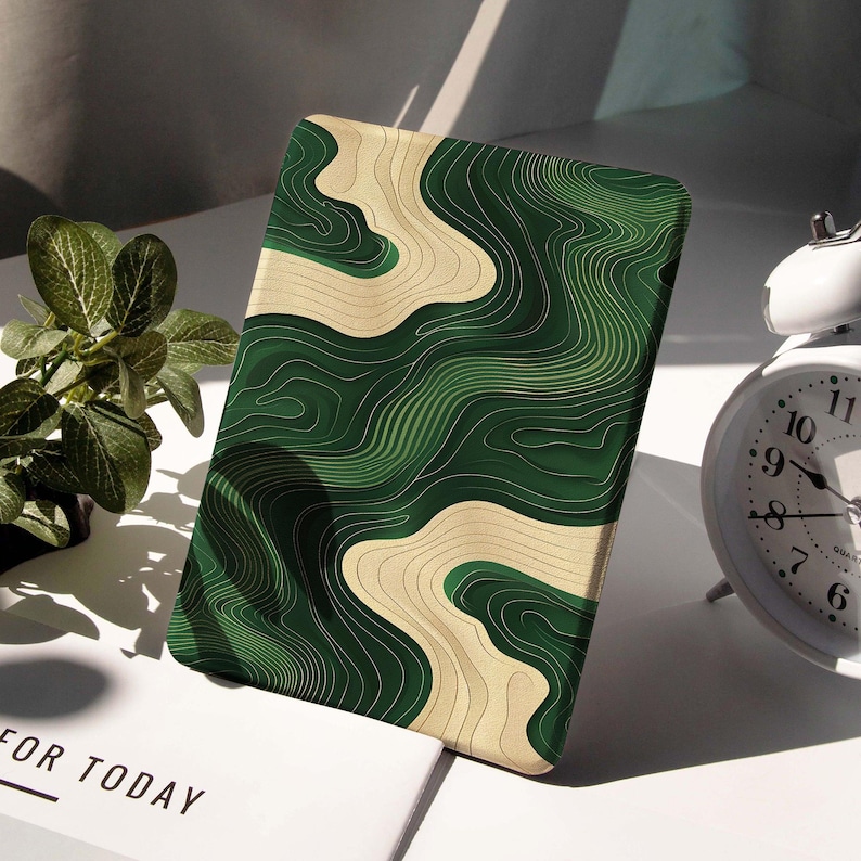 May include: A rectangular case featuring a green and beige topographic design. The case has a curved, layered pattern in shades of green and beige. The text "FOR TODAY" is visible on a white surface in the background.