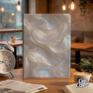 May include: A rectangular tablet case with a pearlescent, swirling design in white, gold, and iridescent hues. The case is displayed on a wooden table, next to a cup of coffee and an open book. The text "Case Crafter" is visible.
