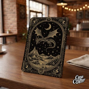 Può includere: Custodia nera per tablet con un design di drago dorato, una luna crescente e un paesaggio montano. La custodia ha un bordo ornato con stelle e il testo "Case Crafter". Esposta su un tavolo di legno.