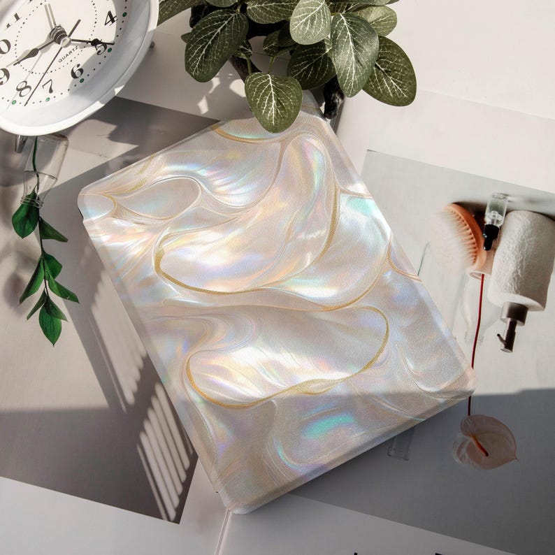Op de afbeelding: Een parelmoer, rechthoekige hoes met een wervelend, iriserend ontwerp en goudkleurige rand. De hoes reflecteert licht en toont een scala aan kleuren. Waarschijnlijk voor een tablet of ander elektronisch apparaat.