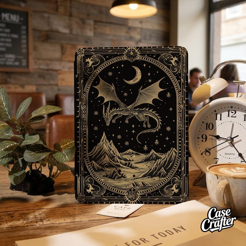May include: A black rectangular tablet case featuring a gold-toned illustration of a dragon flying over a mountain range under a crescent moon and stars, enclosed within an ornate decorative border with intricate line work and geometric patterns.