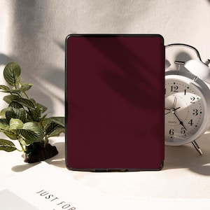 May include: A burgundy tablet case with a black border. The case is rectangular and has a solid color. A white analog alarm clock and a small green plant are in the background. The text "JUST FOR" is partially visible.