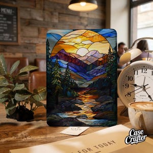 May include: A colorful stained-glass design featuring a mountain landscape with a setting sun, river, and trees. The artwork is displayed on a rectangular object, possibly a phone case or tablet cover. The image has a warm color palette.