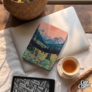 May include: A rectangular e-reader case featuring a printed landscape illustration of snow-capped mountains, a dense pine forest, and a vibrant meadow filled with colourful wildflowers under a soft pink and peach-toned sky.