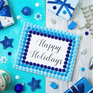 May include: A rectangular sign with the text Happy Holidays in black script, framed by rows of light blue and dark blue pom-poms. The sign is surrounded by blue and white gift boxes, blue ornaments, white snowflake cutouts, and a silver menorah.