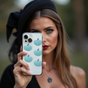 May include: A clear smartphone case featuring five small, raised, light blue pumpkin-shaped decorations arranged vertically and diagonally across the back surface, with a visible camera lens cutout in the upper left corner of the protective cover.