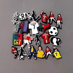 May include: A collection of colorful soccer-themed charms and accessories. Includes soccer balls, jerseys with the number 7, player silhouettes, and the text "CRA" and "IS LIFE". The charms feature red, white, black, yellow, and blue colors.