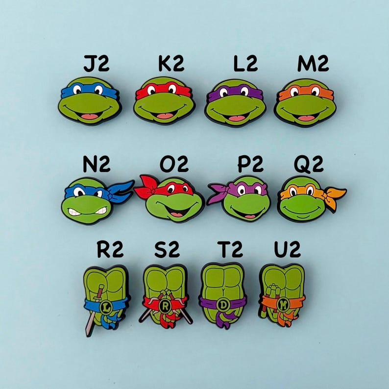 May include: A collection of green Teenage Mutant Ninja Turtle-themed shoe charms. Each charm features a different character with a colored mask and initial. The charms are in various shapes and sizes, with a light blue background.