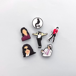 May include: A collection of six black and white pop culture-themed charms. The charms depict various poses and images of a famous singer, including a silhouette with the text "THE KING".
