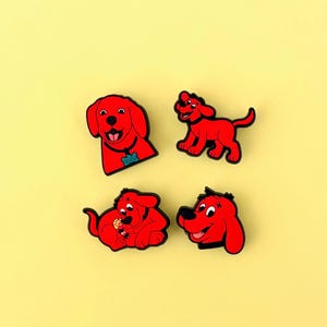 May include: Four red dog-shaped charms with black outlines are arranged on a yellow background. The charms depict a smiling dog in different poses. One charm has a blue tag that says "Clifford".