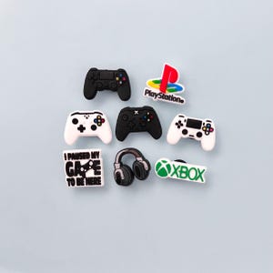May include: A collection of gaming-themed charms, including black and white game controllers, a PlayStation logo, an Xbox logo, a pair of headphones, and a charm that says "I paused my game to be here."