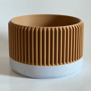 Puede incluir: Una maceta cilíndrica con una parte superior amarilla mostaza acanalada y una parte inferior blanca moteada.