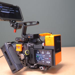 Könnte beinhalten: Professionelles Video-Kamera-Setup mit montiertem Monitor, in Schwarz und Orange. Die Kamera zeigt Einstellungen auf einem kleinen Bildschirm an, und der Monitor zeigt eine Benutzeroberfläche. Das Setup umfasst diverses Montagezubehör.