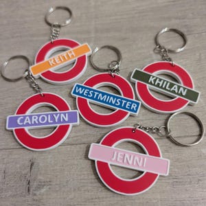 May include: Five red and white London Underground-style keyrings with different coloured bands and names: Keith, Westminster, Khillan, Carolyn, and Jenni.