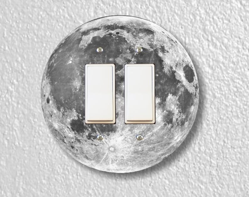 May include: A round light switch cover with a black and white image of the moon. The cover has two white toggle switches.