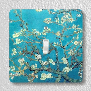 May include: A light switch cover featuring a painting of a blooming almond tree with white flowers against a vibrant blue sky. The painting is reminiscent of the style of Vincent van Gogh.