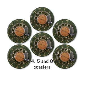 May include: Six green and gold rotary phone dial coasters with the numbers 4, 5 and 6 printed on the bottom. Each coaster has a gold dial with the letters and numbers of a rotary phone dial. The center of each dial has a small, round, brown label with the text "638-4796" printed on it.