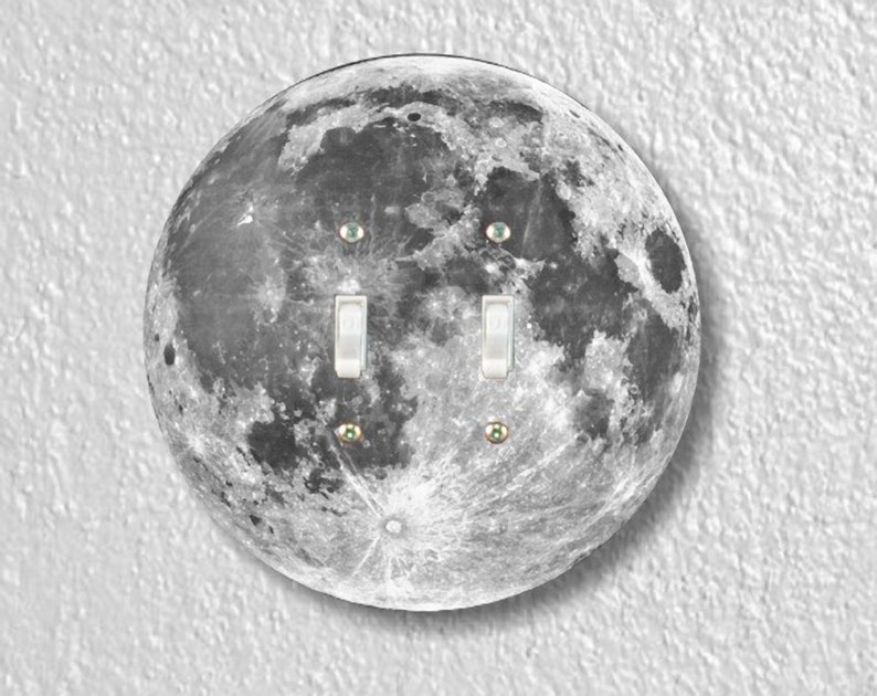 May include: A round light switch cover with a black and white image of the moon. The switch cover has two toggle switches.