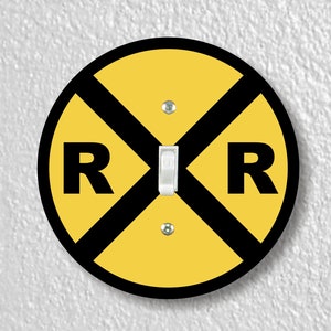 May include: A round yellow light switch cover with a black railroad crossing sign and the letters "RR" in black.