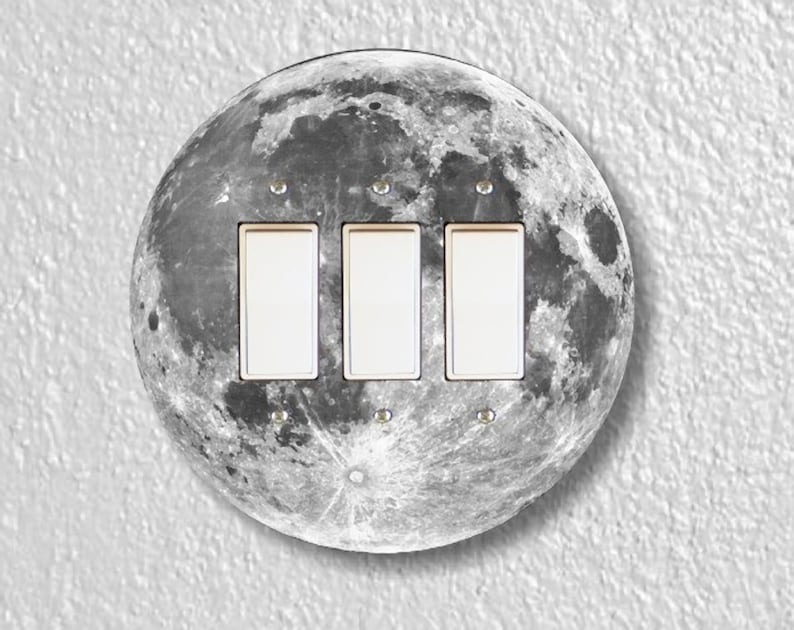 May include: A round light switch cover with a black and white image of the moon. The cover has three toggle switches.