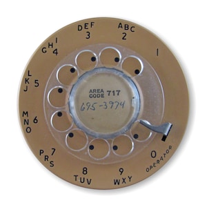 May include: A gold rotary dial phone with a clear plastic faceplate. The dial has black numbers and letters. The area code 717 and phone number 695-3974 are visible in the center of the dial.